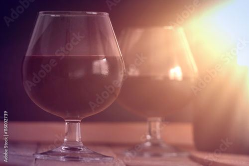Two wine glass and a bottle on a wooden table against a black background. Sun light. Empty copy space for editor's text.