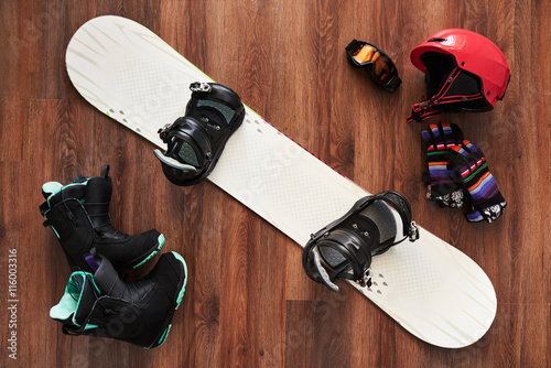 set of snowboard boots, helmet, gloves and mask on wooden