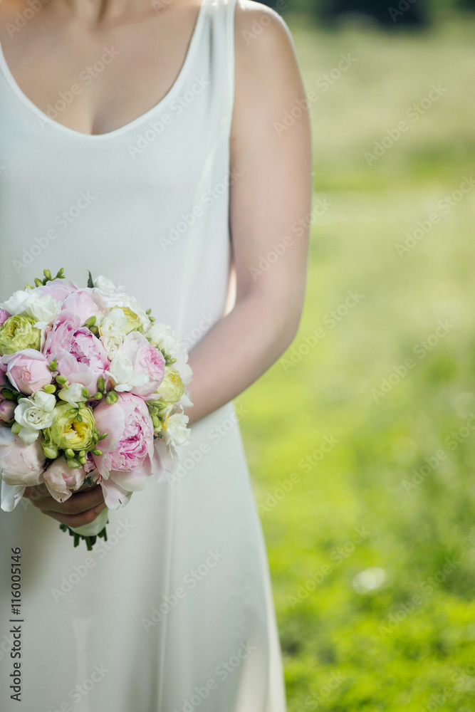 Bride holding a wedding bouquet of fresh peonies, roses and freesias. 