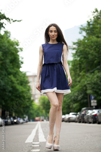 Young beautiful woman in a blue short dress walking on the road