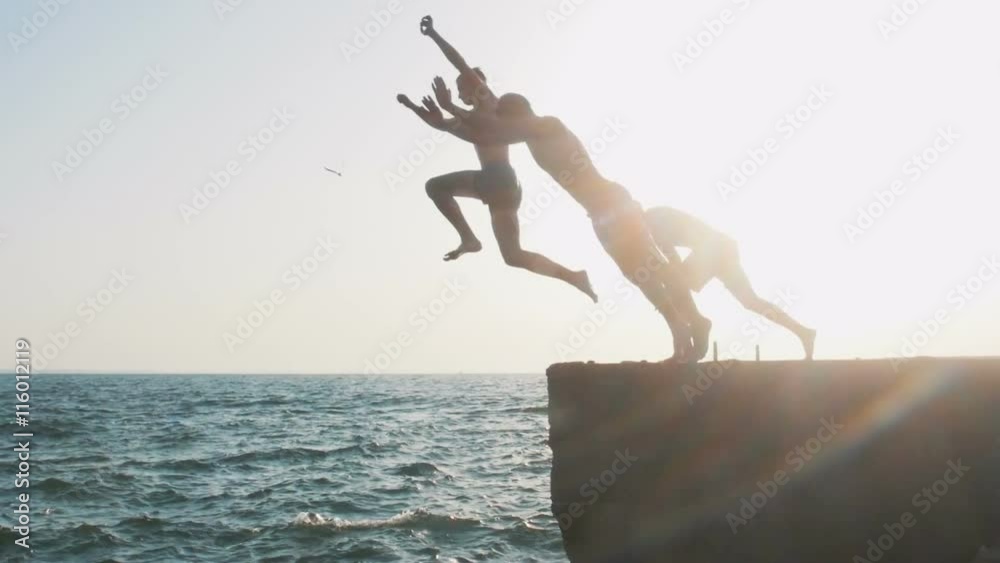 Group of friends running and jumping off sea pier in the water, slow motion