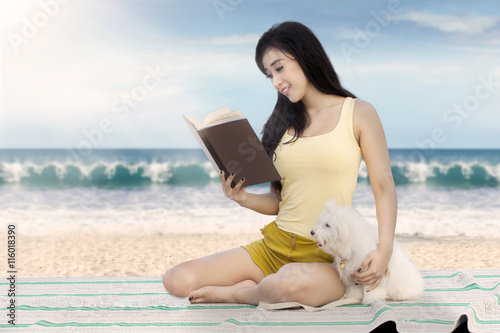 Pretty model with dog reads book at shore