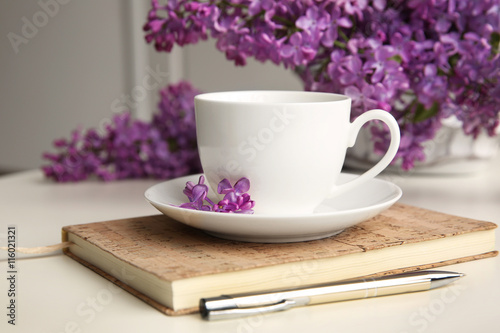 Purple lilac flowers and cup on white table