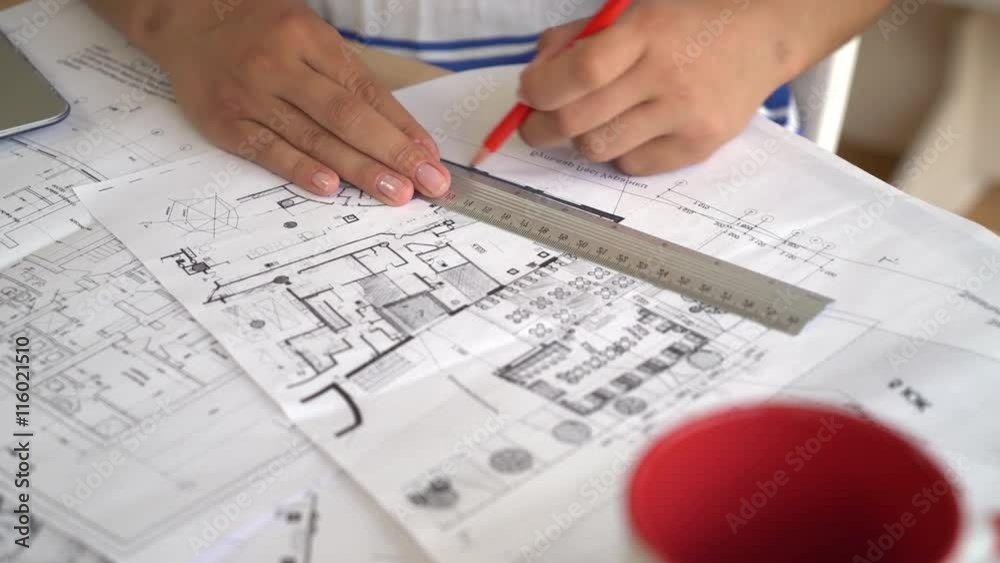 Woman architect correct design and draftsmanship on architectural sketch. On the wooden desk plan new building or house or flat. She using red pencil and line.Mixed race women's hands drawing on
