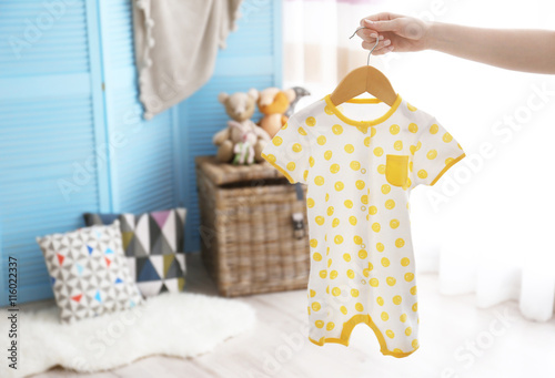 Female hand holding baby bodysuit in interior of child's room photo