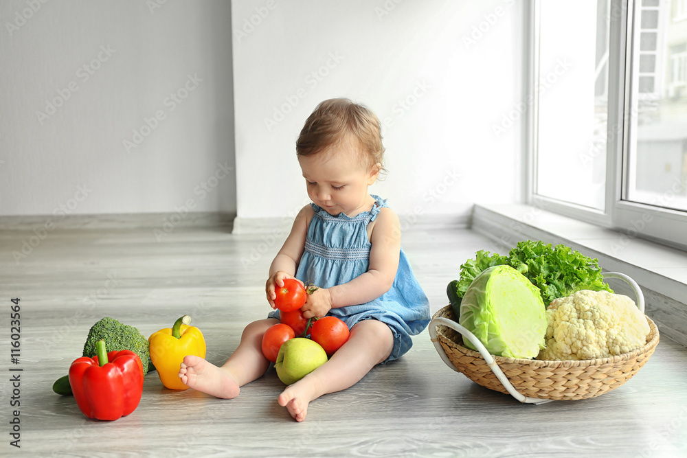 Cute baby girl with vegetables on wooden floor Cute baby girl with vegetables on wooden floor