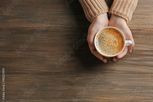 Female hands holding cup of coffee on wooden background photo
