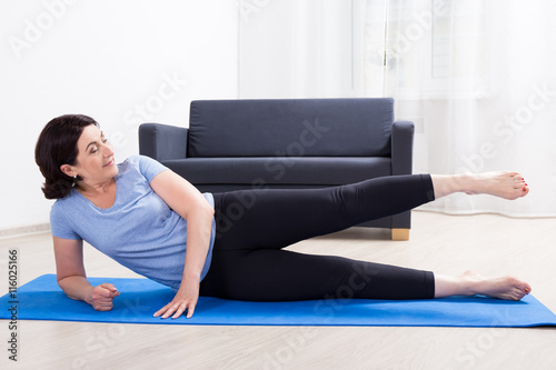 slim sporty mature woman doing stretching exercises on yoga mat