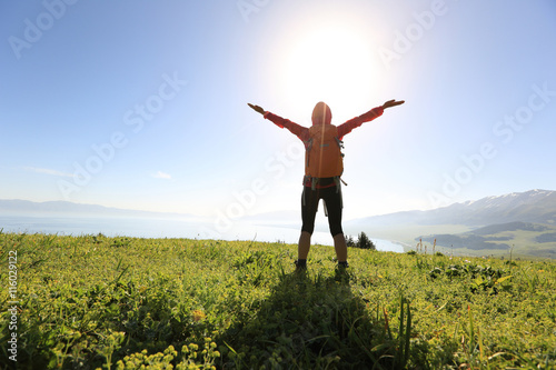 cheering young woman backpacker open arms at mountain peak