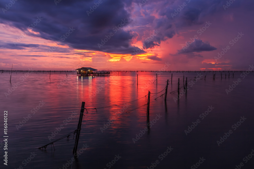 Dark clouds over lake with red sky and wooden hut on surface at sunset