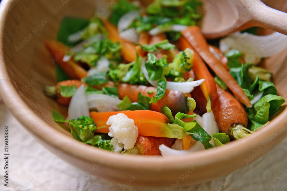 Fresh vegetable salad with baby carrot in wooden bowl closeup