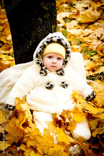 little girl sitting under a  tree on yellow leaves in the Park. Enjoying his first autumn. Emotions baby. Nice warm weather