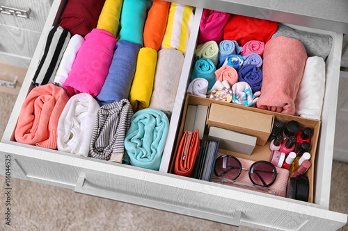 Neatly folded clothes with accessories in chest of drawers photo