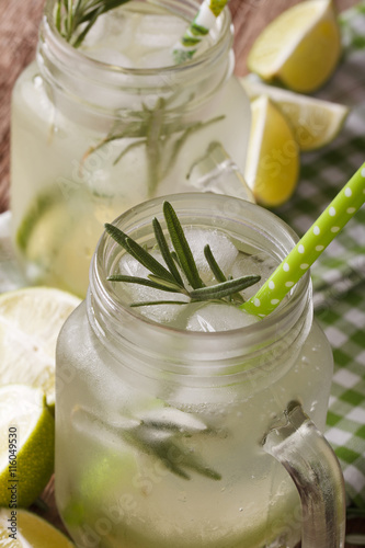 Cold cocktail with lime, ice and rosemary macro in a jar. vertical 
