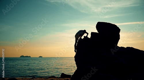 Man climbs on a rock at sunset on the beach-1