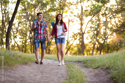 Young Couple Man and Girl in casual Travel Clothing with Backpacks walking on Forest Trail talking and enjoying sightseeing