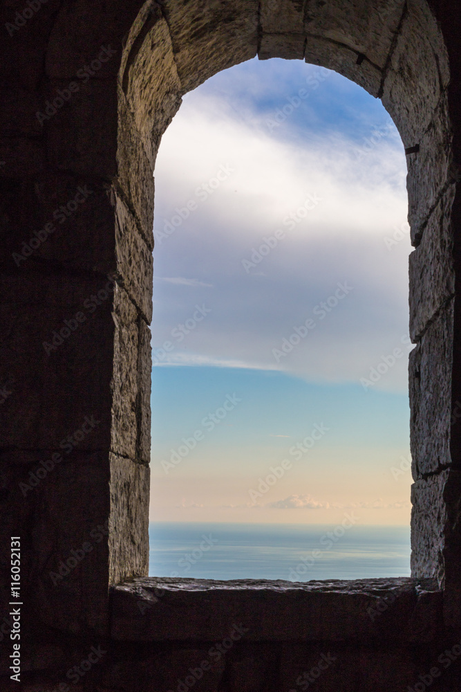 View at blue sky from ancient arch window in stone wall