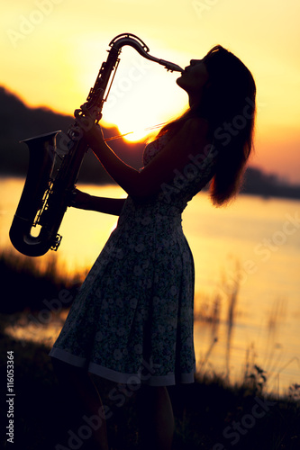 Photography portrait of a woman in a dress playing the saxophone near the river