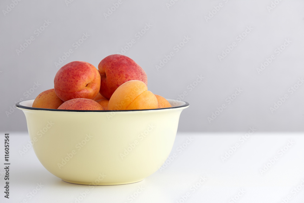 Ripe apricots in yellow bowl on white table Ripe apricots in yellow bowl on white table
