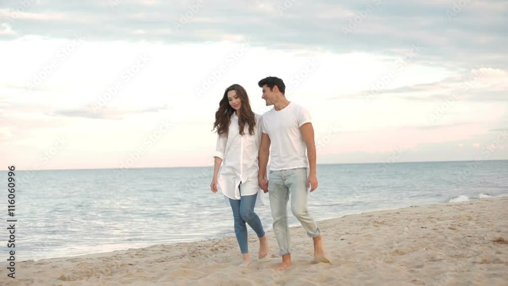 Young romantic beautiful couple walking on the beach and talking Young romantic beautiful couple walking on the beach and talking