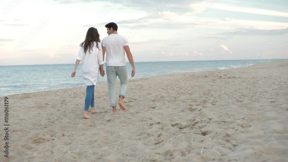 Back view of a young romantic couple walking at the beach and holding hands Back view of a young romantic couple walking at the beach and holding hands