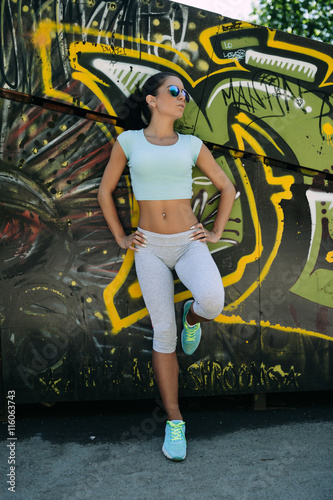 Attractive fit young woman, getting ready for jogging, posing in front of graffiti wall