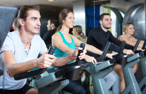 Young adults on exercise bikes in gym.