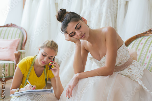 Obraz na plátně Tired bride with wedding assistant in tailor shop working on dress