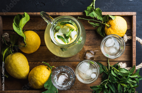 Jug and glasses with homemade lemonade, ice cubes on wooden tray, top view