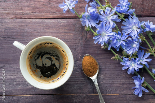 Chicory herbal drink and blue flowers on wooden table. Spoon with root powder. Top view photo