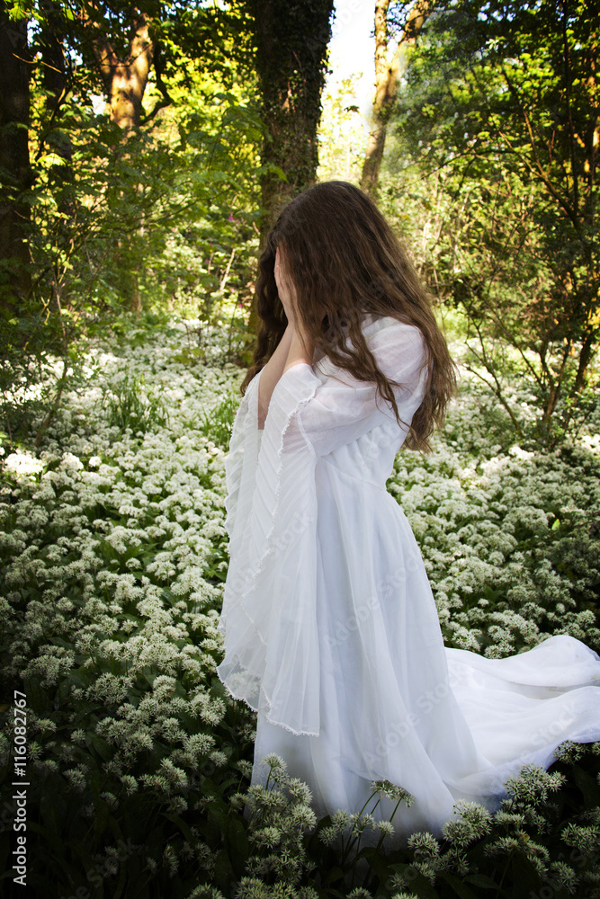 Woman wearing a long white dress standing in a forest Woman wearing a long white dress standing in a forest