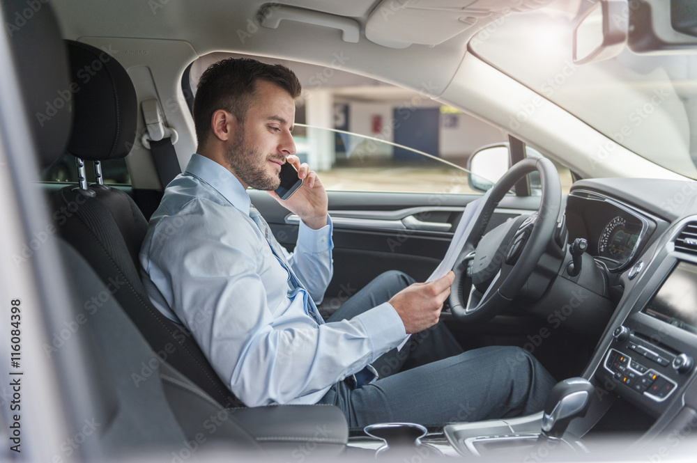 Businessman with documents on cell phone in car Businessman with documents on cell phone in car
