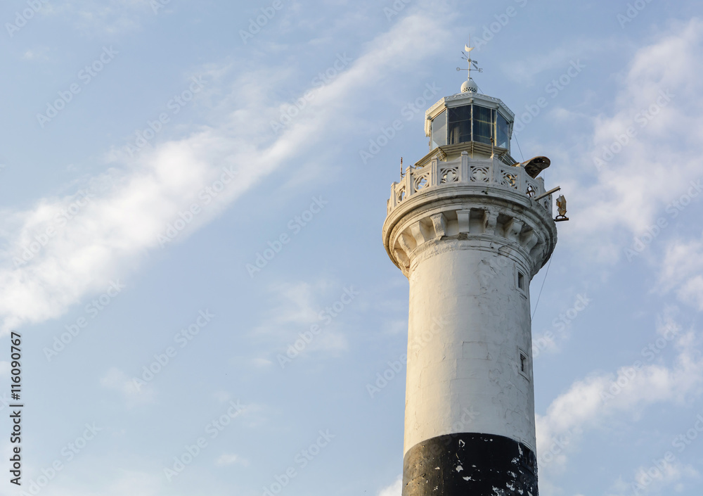 high white stone lighthouse with a black stripe on a blue evening sky with clouds