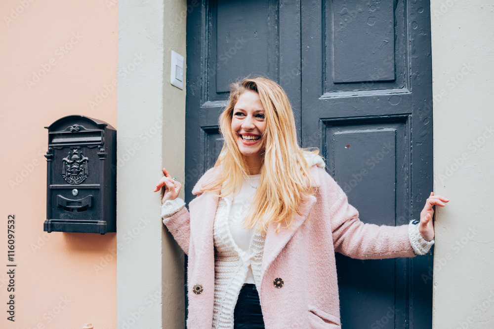 Fototapeta premium young beautiful caucasian blonde hair woman standing on the front door, overlooking smiling - happiness, having fun, smiling concept