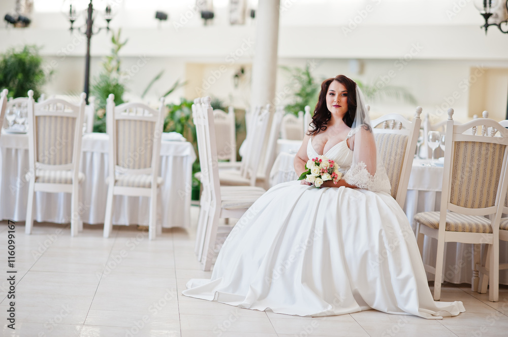Big breasts brunette bride with wedding bouquet sitting on chair Big breasts brunette bride with wedding bouquet sitting on chair