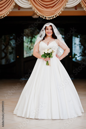 Big breasts brunette bride with wedding bouquet posed at wedding