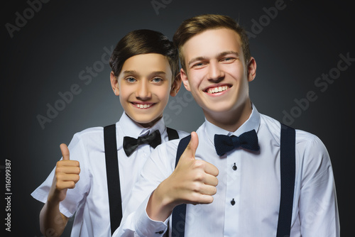 Closeup portrait of two successful happy boys show thumbs up isolated grey background. Positive human emotion.