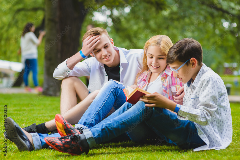 Smiling kids having fun and reading book at grass. Children playing outdoors in summer. teenagers communicate outdoor Smiling kids having fun and reading book at grass. Children playing outdoors in summer. teenagers communicate outdoor