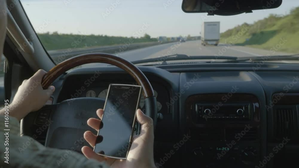Over the shoulder shot of a man using his phone while driving on a busy road.
