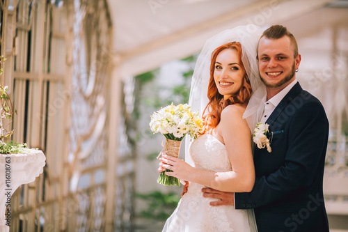 Happy couple of newlyweds valentynes posing and hugging in old europeand street with bouquet. Vintage cafe. Woman with red hair. Newlywed kiss. Flowers boquet in hand. Copy space. photo