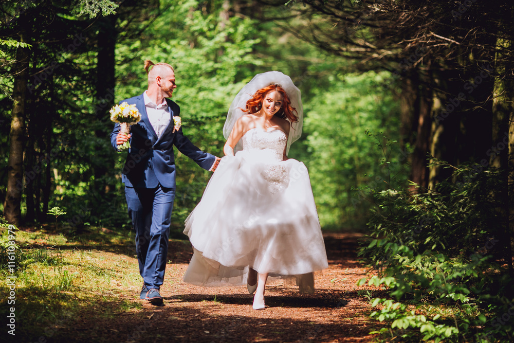Newlyweds run along the path in the park on the evening. Bride with ore hair