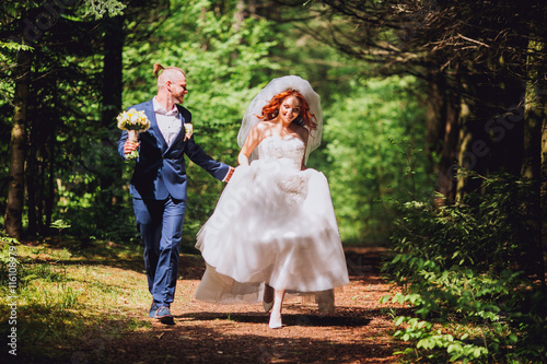 Newlyweds run along the path in the park on the evening. Bride with ore hair