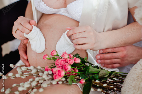 pregnant woman holding little socks on his belly in white underwear