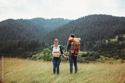A couple hikers Hiking with backpacks walk along a beautiful mountain area holding hands . The concept of active rest