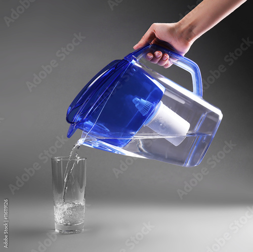 Female hand pouring water into glass on grey background