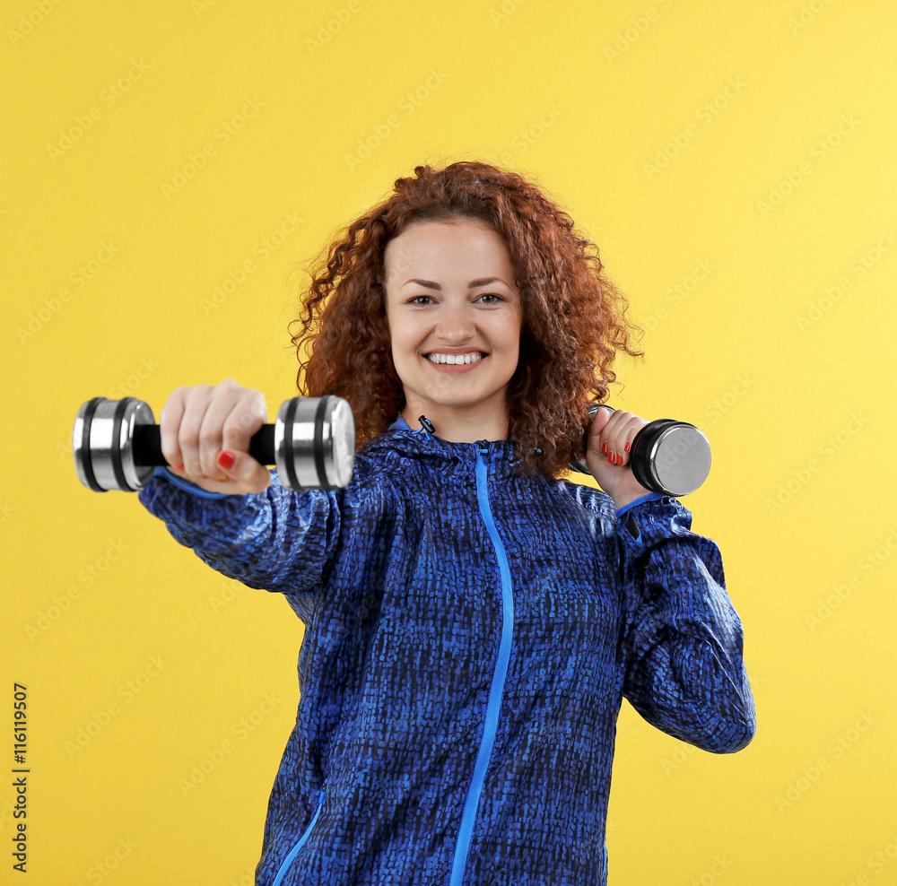 Obraz premium Attractive woman exercising with dumb bells on yellow background