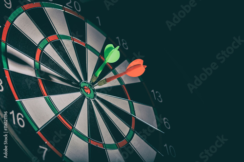 Two darts in the target center, bullseye, black background, copy space