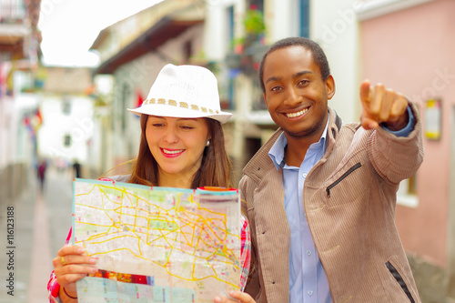 Interracial happy couple wearing casual clothes in urban envrionment, interacting and looking at map photo
