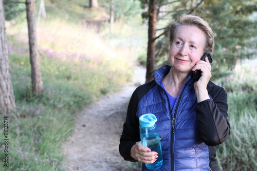 Close-up portrait of a smiling mature woman using mobile phone in the forest with copy space