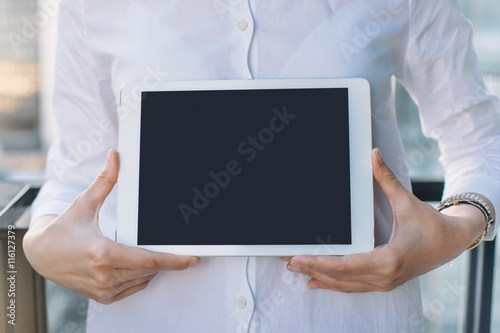 Close-up of businesswoman's hands showing digital tablet with blank screen. Businesswoman in white shirt using modern tablet outdoors. Mock-up of template tablet. Shallow DOF